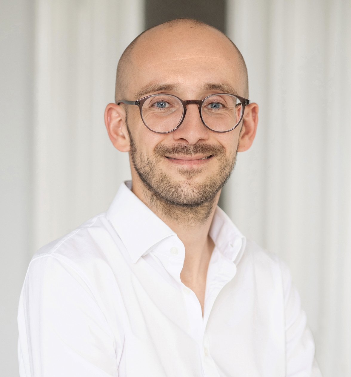 Portraitfoto-Benno-Legler Auf dem Bild ist Benno Legler zu sehen. Er lächelt, trägt eine Brille und ein weisses Hemd.